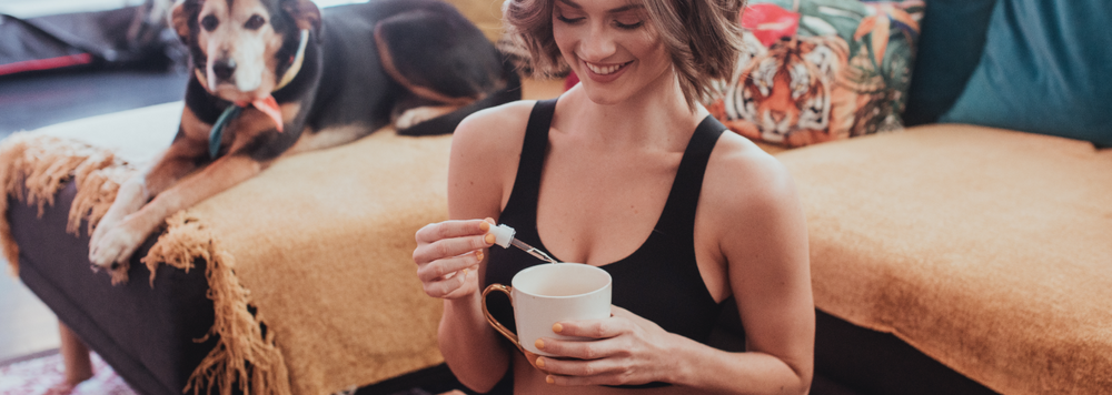 woman putting drops of CBD into her tea